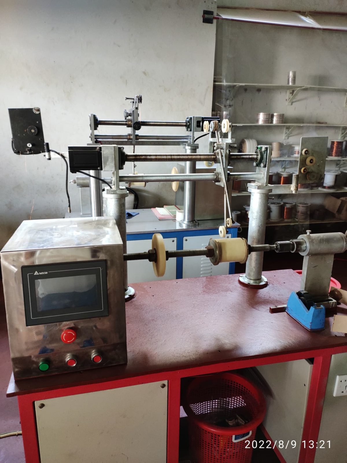 Automatic coil winding machine with a touch-screen controller, stepper motors and shelves of copper wire spools behind