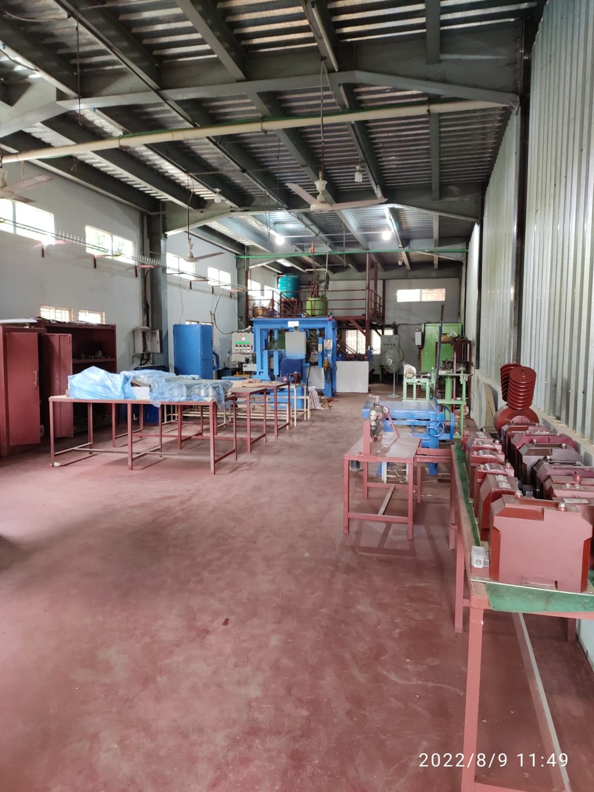 Long production hall with rows of red resin-cast instrument transformers on a bench and machinery in the background