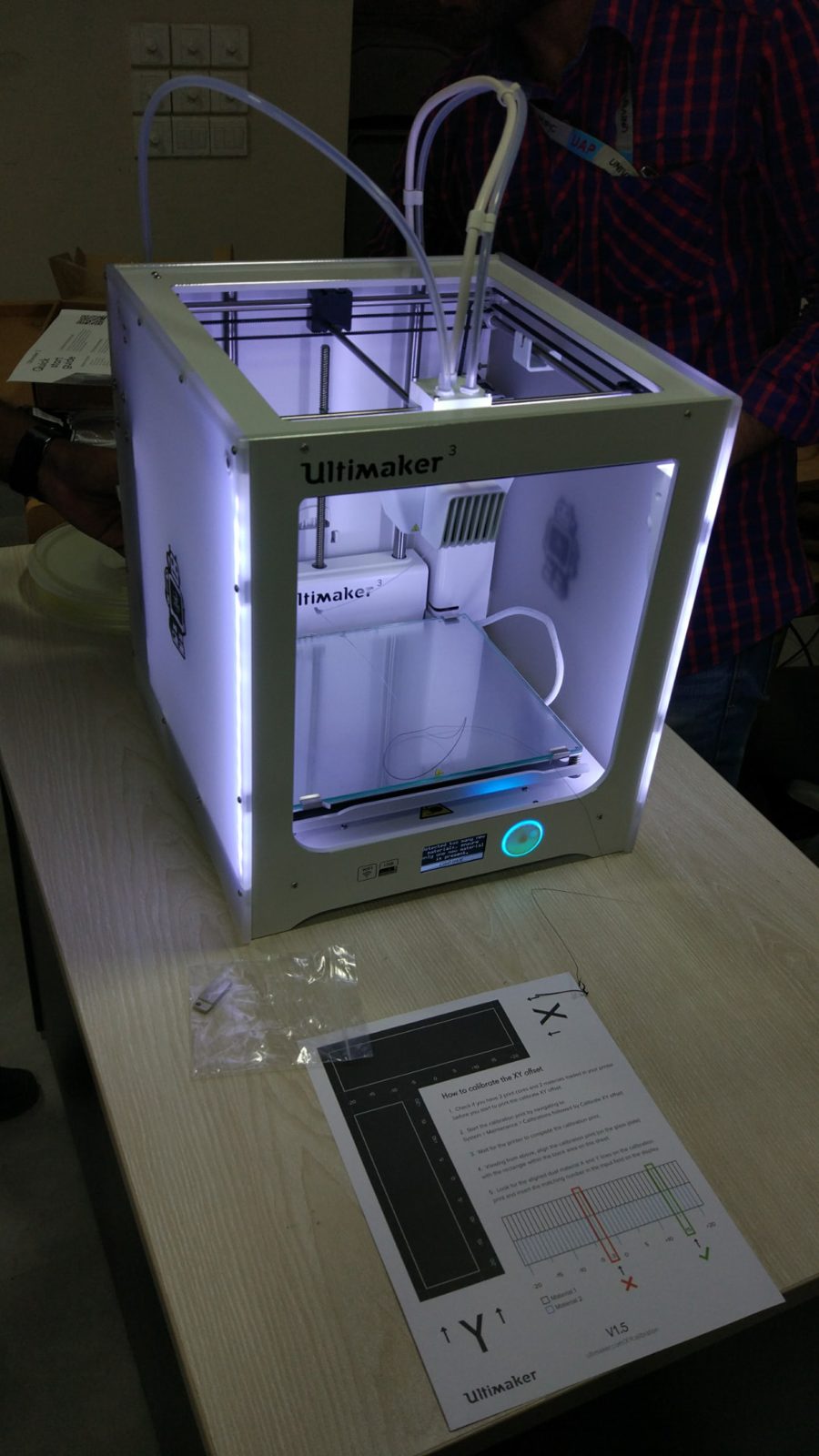 Ultimaker 3 3D printer lit up on a table, with its XY offset calibration sheet in front