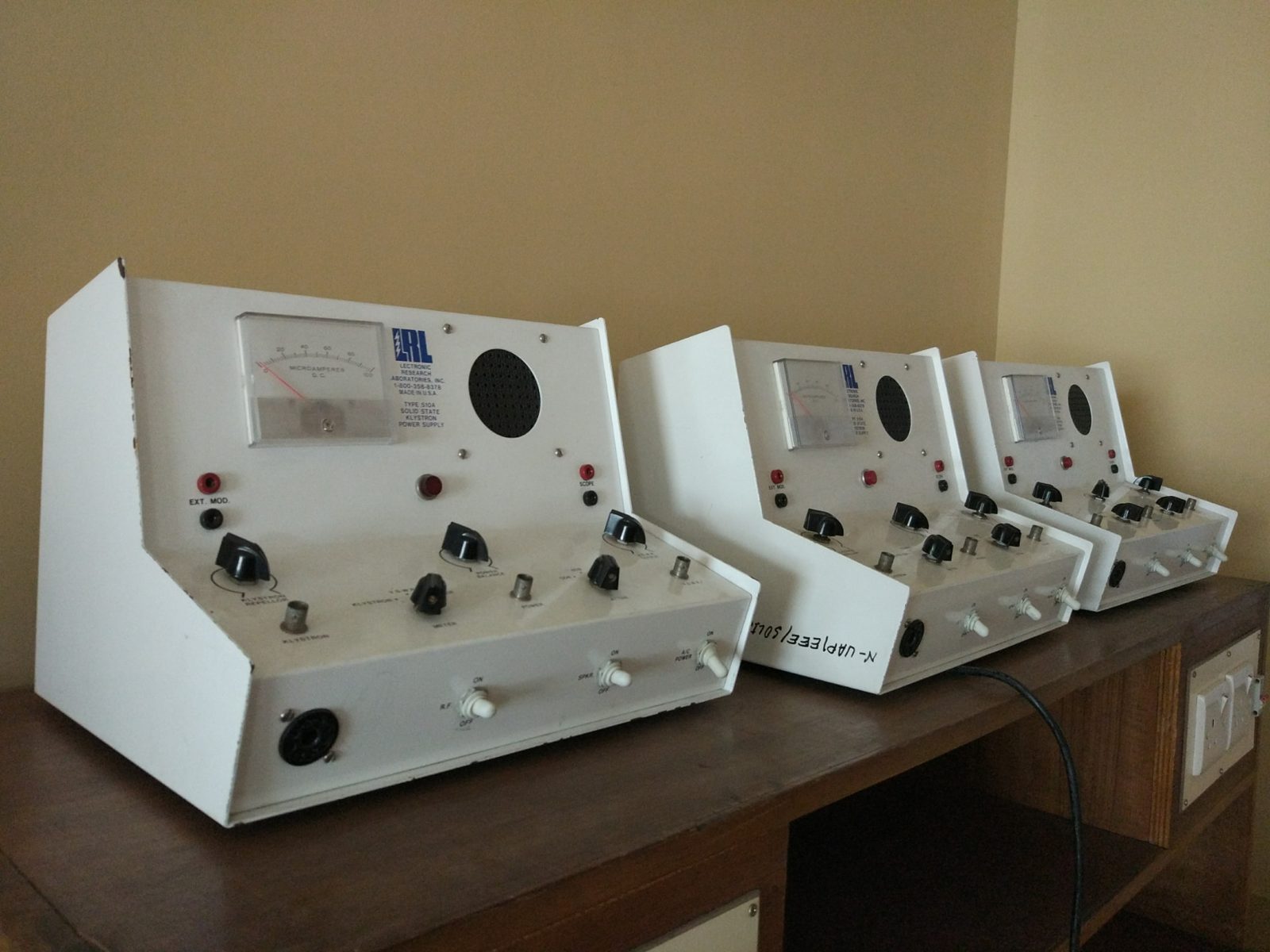 Three solid-state klystron power supplies with analogue microampere meters lined up on a bench