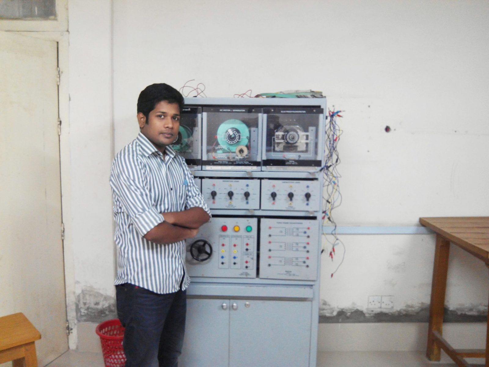 Md Abdul Wahab standing next to an electrical machines training panel with a DC motor/generator, electrodynamometer and load modules